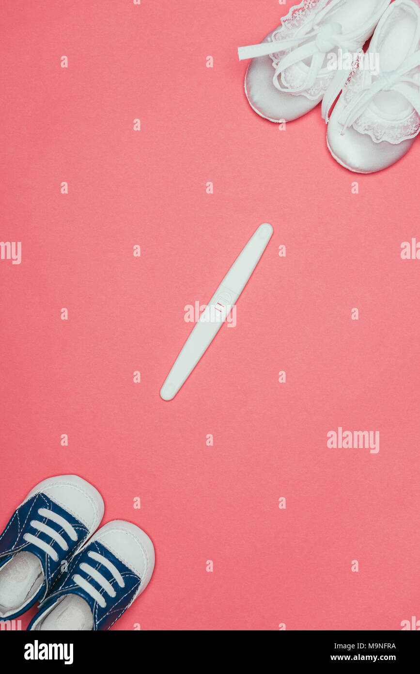 top view of arrangement of  childish shoes and pregnancy test isolated on pink Stock Photo