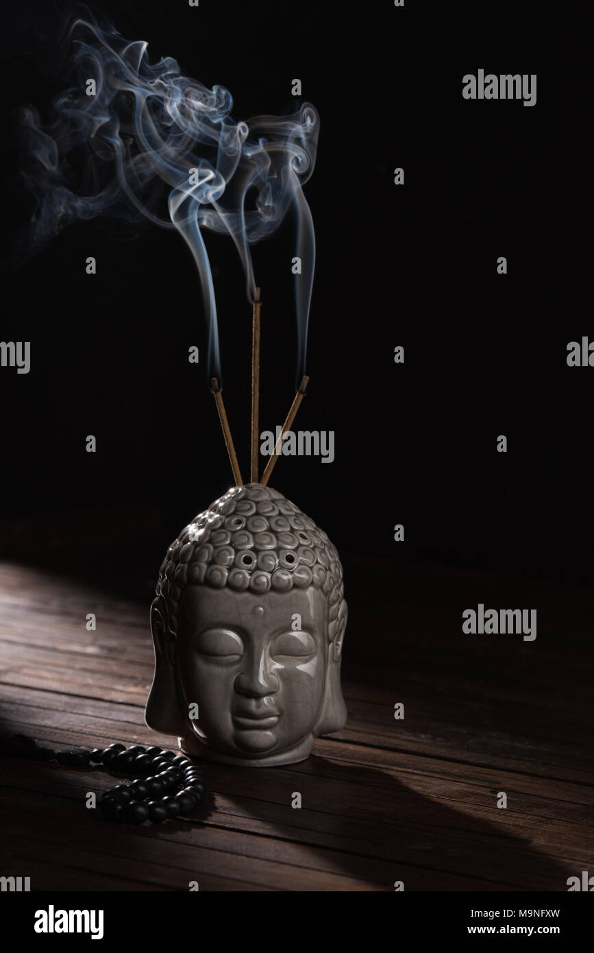 sculpture of buddha head with burning incense sticks Stock Photo