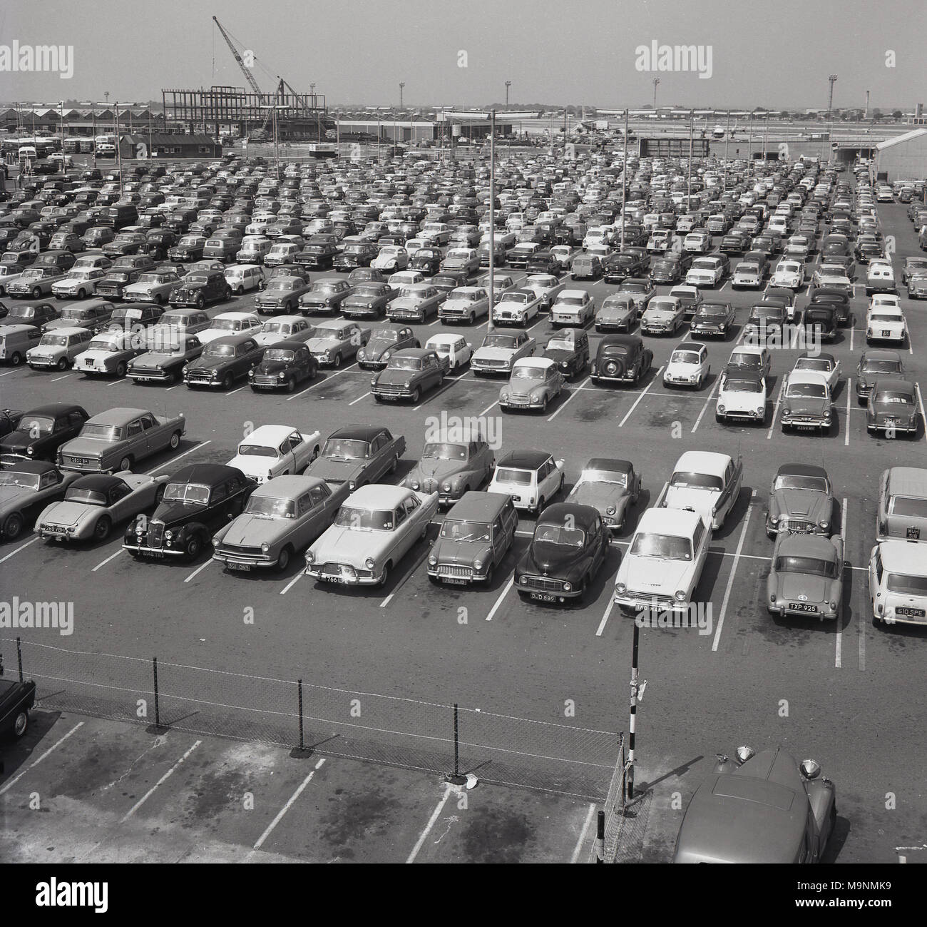 1960s, historical, a large number of cars parked at London's Heathrow airport, England, UK. In the distance is the road vehicle subway going under the main runway and sponsored by Rothmans tobacco. Originally a private airport, it was requistioned to support the RAF in WW2 and opened to civil aviation in 1946.  Passenger numbers at the airport grew quickly to many millions per year as aviation for the masses took off. Stock Photo