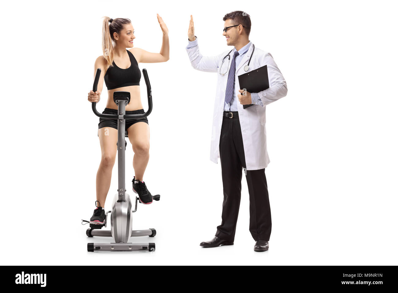 Young woman exercising on a stationary bike and high-fiving a doctor isolated on white background Stock Photo
