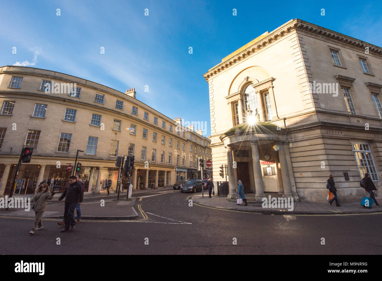 Sunny street scene in Bath at the junction of New Bond Street and Walcot Street with shoppers and cars waiting at traffic lights Stock Photo