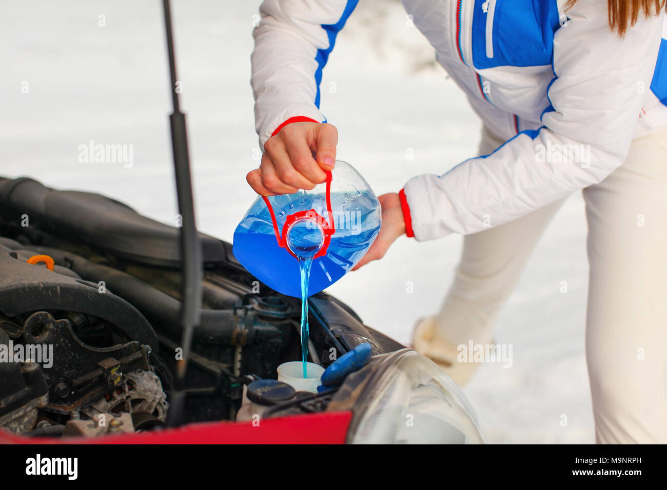 Woman in ski jacket pouring antifreeze car screen wash liquid into dirty car from blue anti freeze water container. Stock Photo