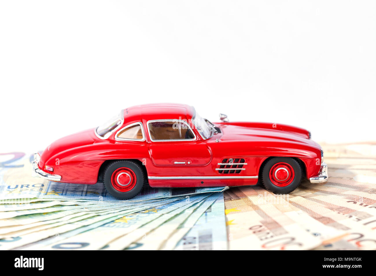 A classic sports car of the year 1954 of red color over euro bills with white background. Stock Photo
