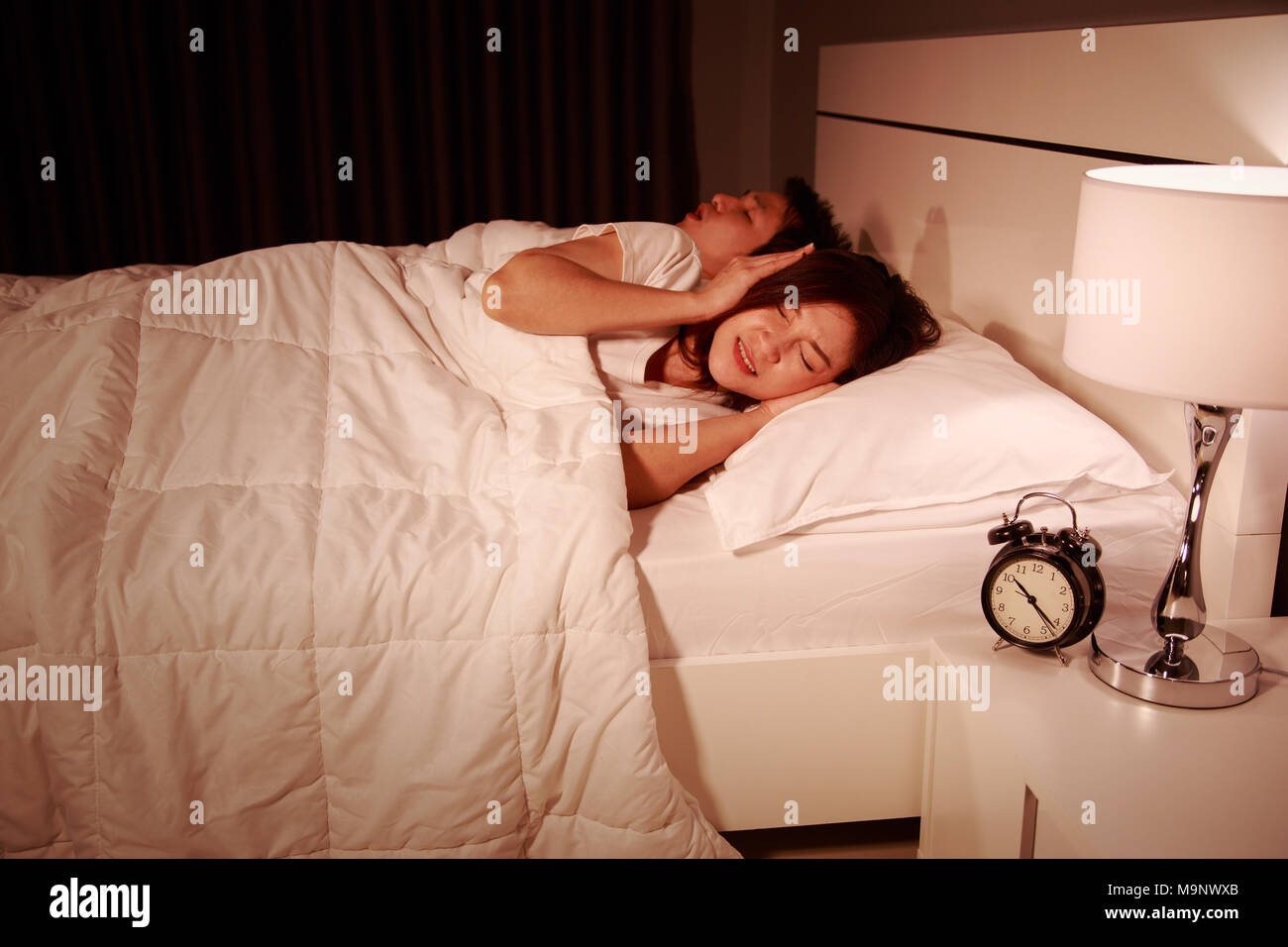 annoyed young wife blocking her ears from noise of husband snoring at night Stock Photo