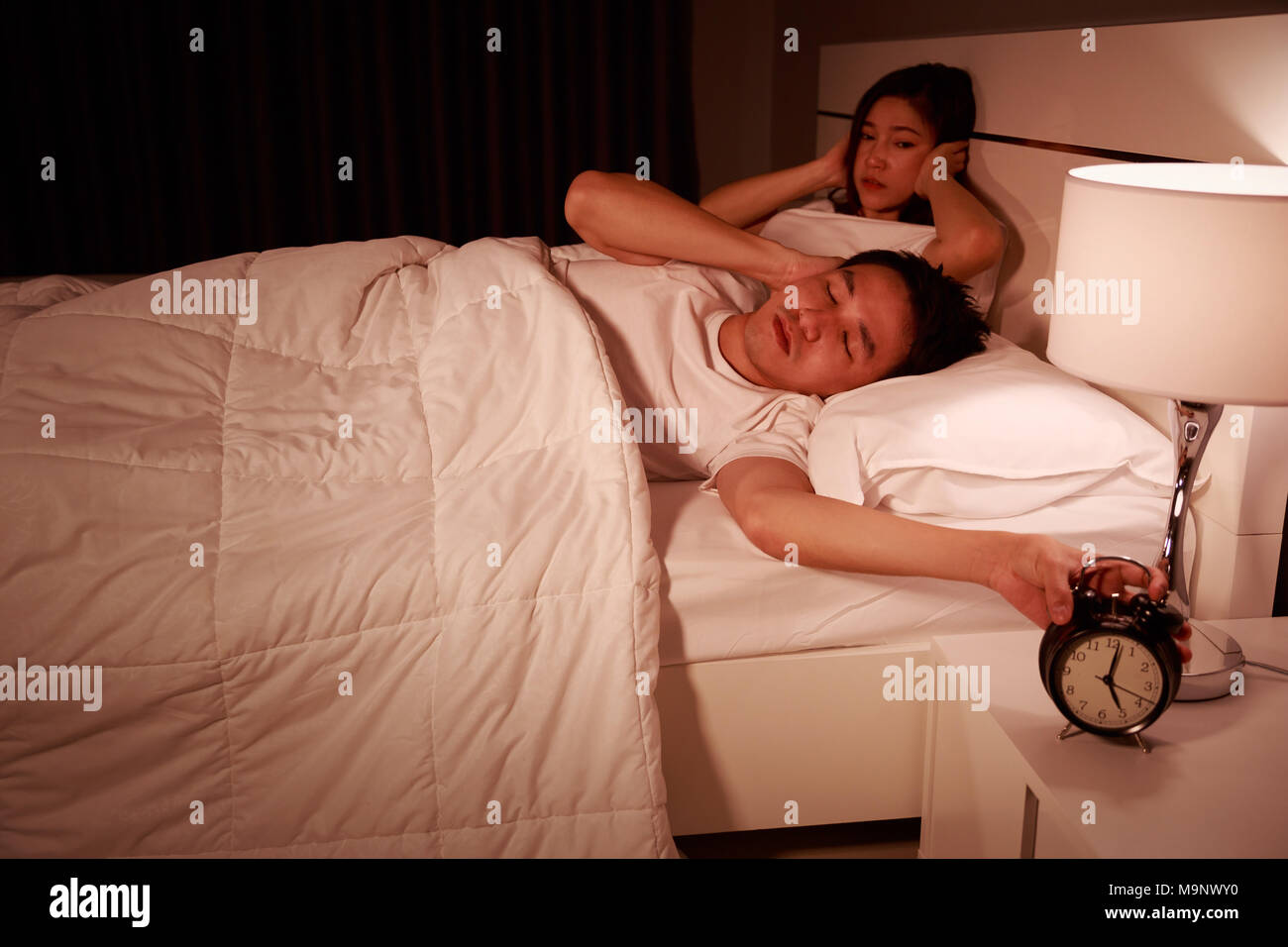 unhappy couple being awakened by an alarm clock in bedroom in the morning Stock Photo
