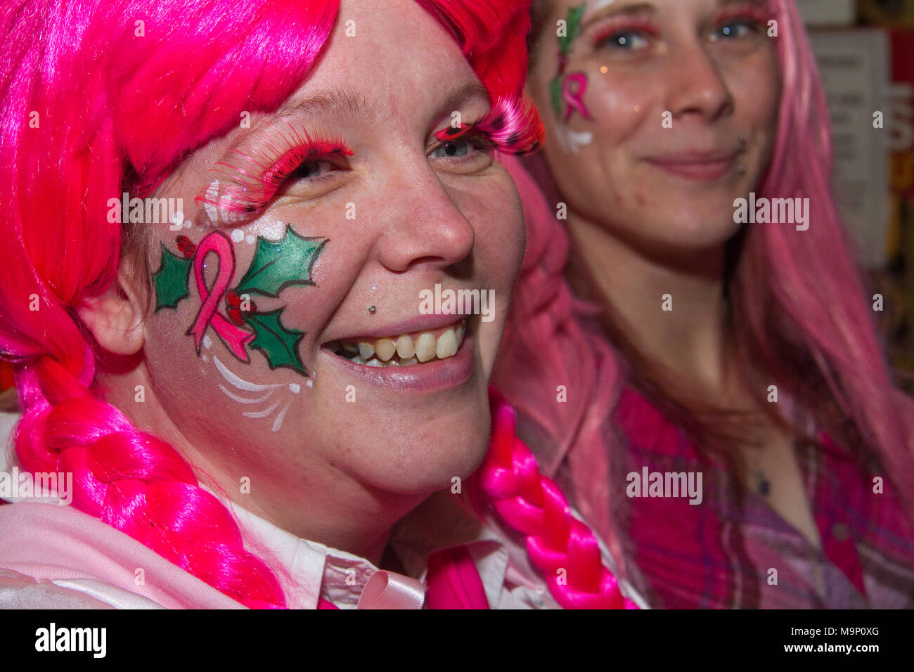 Woman in pink wig with holly painted on her face at a Christmas Fair Stock Photo