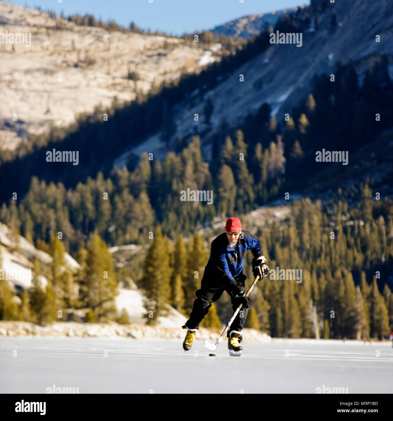 Low angle front view of a ice skater playing ice hockey on a snow free, frozen Tenaya Lake in Yosemite National Park. Stock Photo