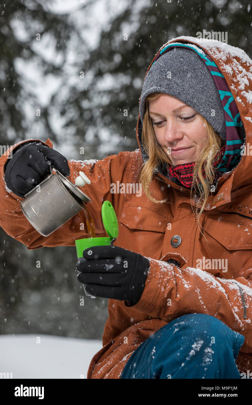 Woman pouring coffee made on camping stove into cup in winter, Sureanu, Romania Stock Photo