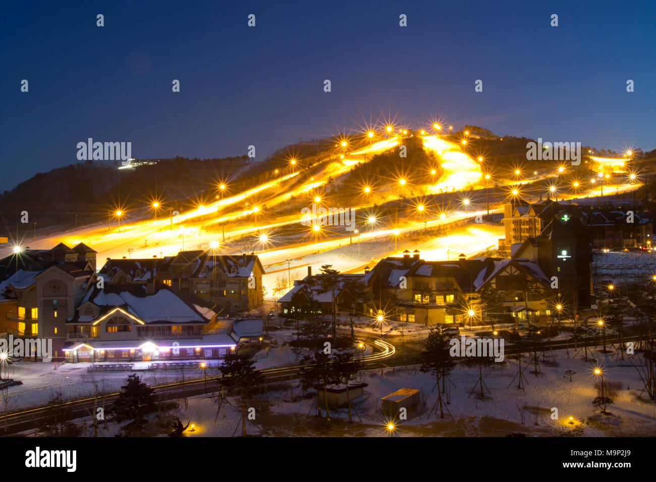 At night the Alpensia resort in the Gangwon-do region of South Korea is lit by lights.  Some South Korean ski resorts offers night skiing for people from Seoul who can only ski after working hours.  The Alpensia Resort is a ski resort and a tourist attraction. It is located on the territory of the township of Daegwallyeong-myeon, in the county of Pyeongchang, hosting the Winter Olympics in February 2018.  The ski resort is approximately 2.5 hours from Seoul or Incheon Airport by car, predominantly all motorway.   Alpensia has six slopes for skiing and snowboarding, with runs up to 1.4 km Stock Photo