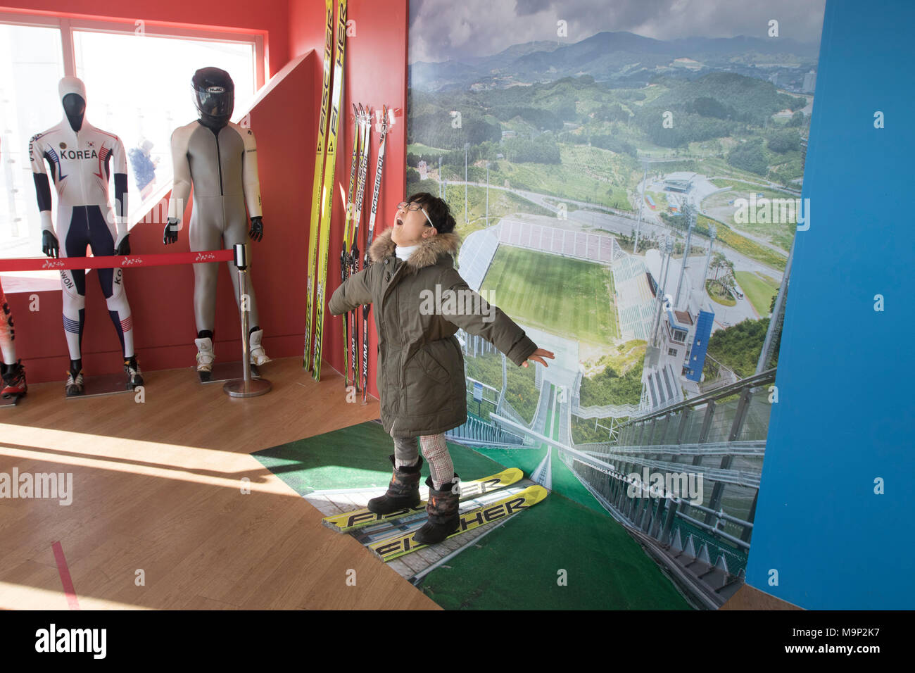 A boy imaginary playing he is flying during a ski jump at the Olympic ski jumping tower of Alpensia resort in South Korea.  The Alpensia Resort is a ski resort and a tourist attraction. It is located on the territory of the township of Daegwallyeong-myeon, in the county of Pyeongchang, hosting the Winter Olympics in February 2018.  The ski resort is approximately 2.5 hours from Seoul or Incheon Airport by car, predominantly all motorway.   Alpensia has six slopes for skiing and snowboarding, with runs up to 1.4 km (0.87 mi) long, for beginners and advanced skiers, and an area reserved for Stock Photo