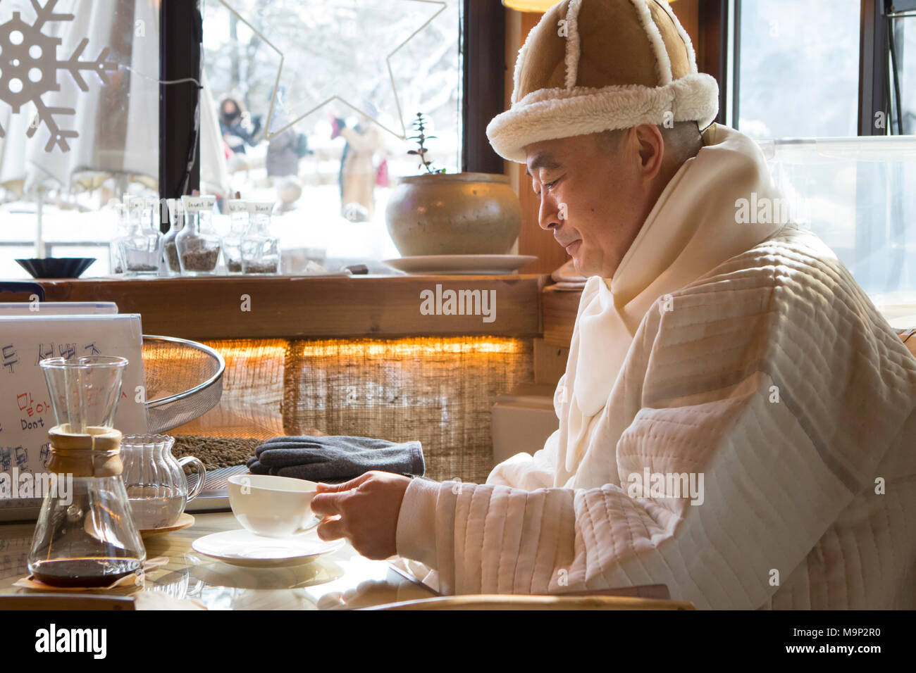 A monk is drinking coffee in the Seolhyang cafe, next to the Buddhist Sinheung-sa temple in Seoraksan National Park, Gangwon-do, South Korea. The name of the cafe means The smell of falling snow, in Korean language.  Seoraksan is a beautiful and iconic National Park in the mountains near Sokcho in the Gangwon-do region of South Korea. The name refers to Snowy Crags Mountains. Set against the landscape are two Buddhist temples: Sinheung-sa and Beakdam-sa. This region is hosting the winter Olympics in February 2018.   Seoraksan is a beautiful and iconic National Park in the mountains near Stock Photo