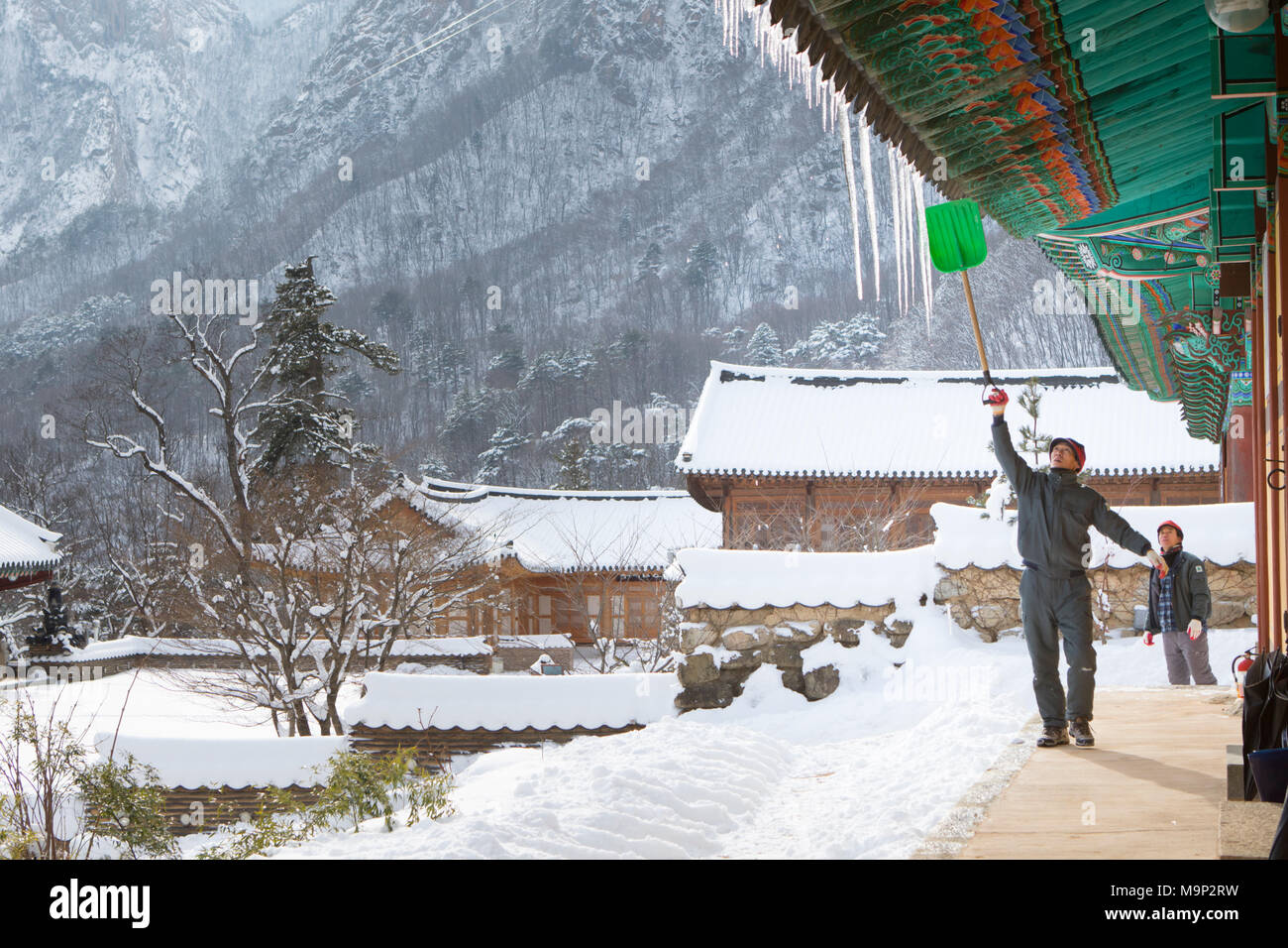 A monk is removing ice from the roof of the Buddhist Sinheung-sa temple in Seoraksan National Park, Gangwon-do, South Korea.  Seoraksan is a beautiful and iconic National Park in the mountains near Sokcho in the Gangwon-do region of South Korea. The name refers to Snowy Crags Mountains. Set against the landscape are two Buddhist temples: Sinheung-sa and Beakdam-sa. This region is hosting the winter Olympics in February 2018.   Seoraksan is a beautiful and iconic National Park in the mountains near Sokcho in the Gangwon-do region of South Korea. The name refers to Snowy Crags Mountains. Set Stock Photo