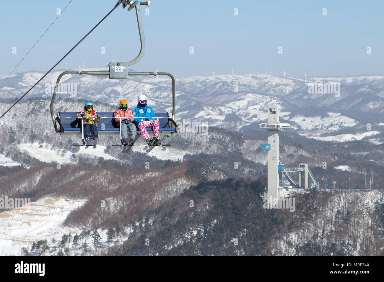Colorful dressed skiers in a chair lift high above Alpensia resort in the Gangwon-do region of South Korea.  The Alpensia Resort is a ski resort and a tourist attraction. It is located on the territory of the township of Daegwallyeong-myeon, in the county of Pyeongchang, hosting the Winter Olympics in February 2018.  The ski resort is approximately 2.5 hours from Seoul or Incheon Airport by car, predominantly all motorway.   Alpensia has six slopes for skiing and snowboarding, with runs up to 1.4 km (0.87 mi) long, for beginners and advanced skiers, and an area reserved for snowboarders. Stock Photo
