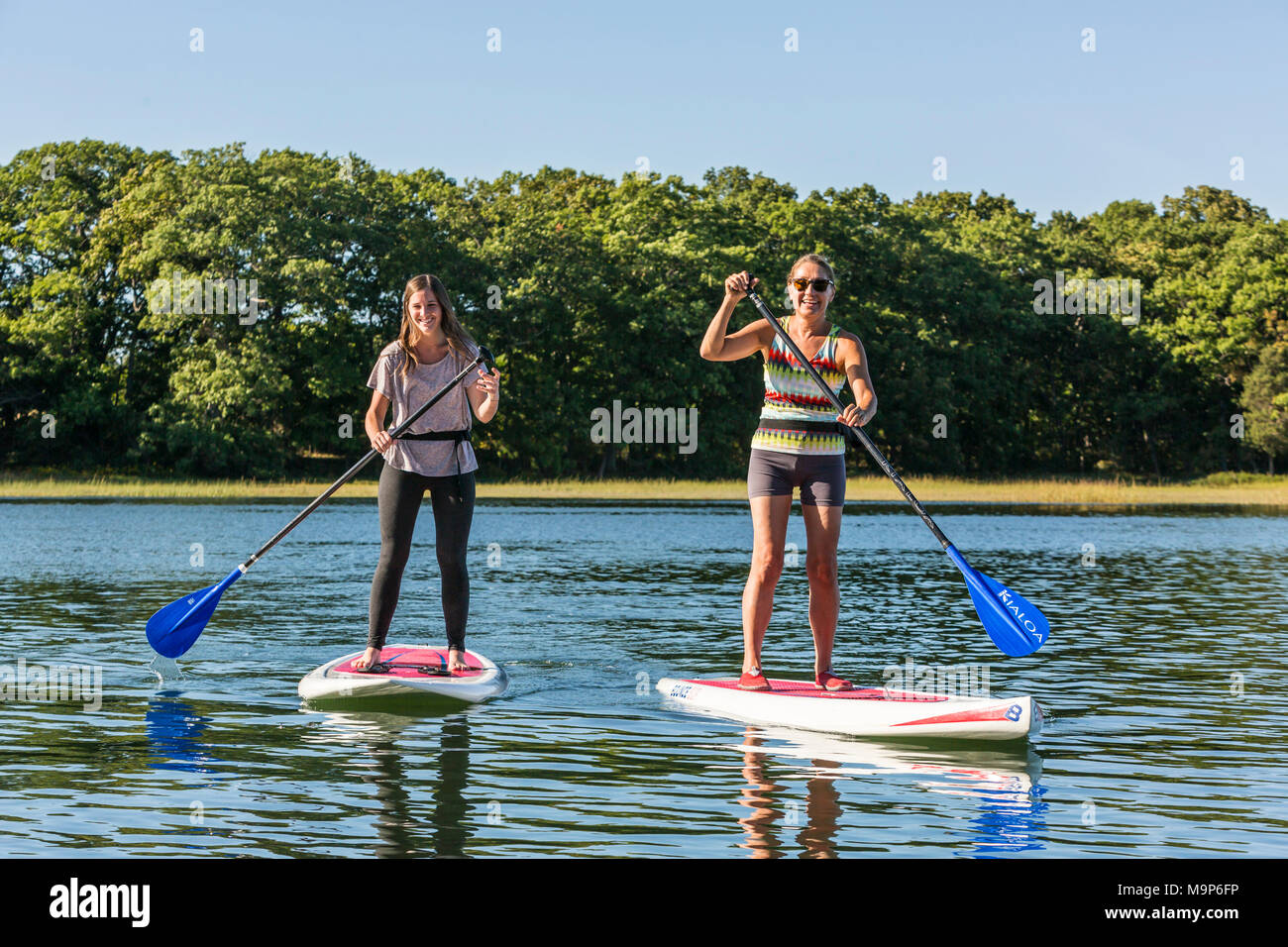 Two women standing up paddle boarding on Essex River at Cox Reservation