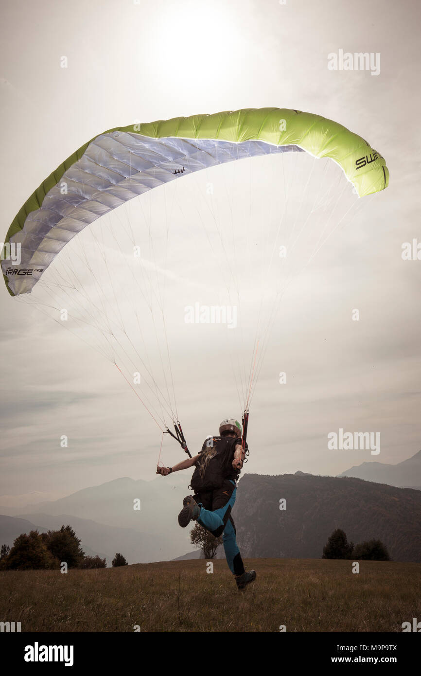 Paraglider landing softly on grass in front of hills, Brento, Venetien, Italy Stock Photo