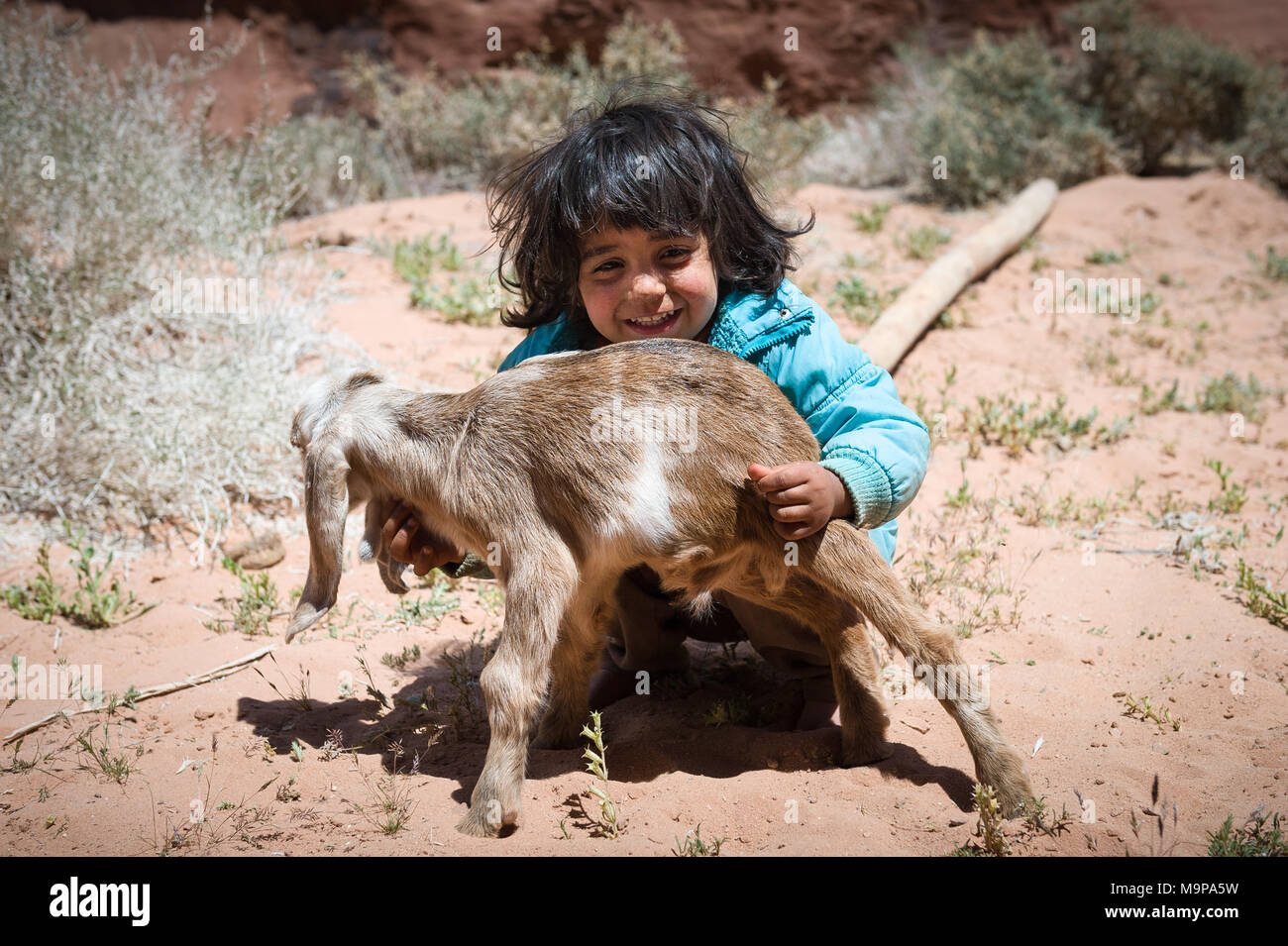 Young Bedouin girl playing with baby goat in the Wadi Rum desert near the border of Saudi Arabia. Stock Photo