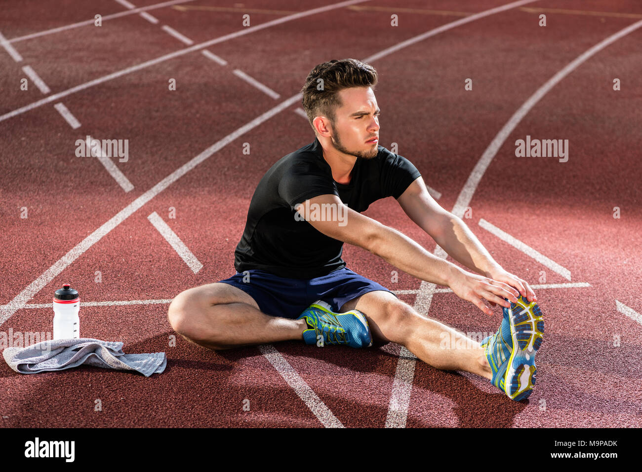 Athlete stretching on racing track before running Stock Photo