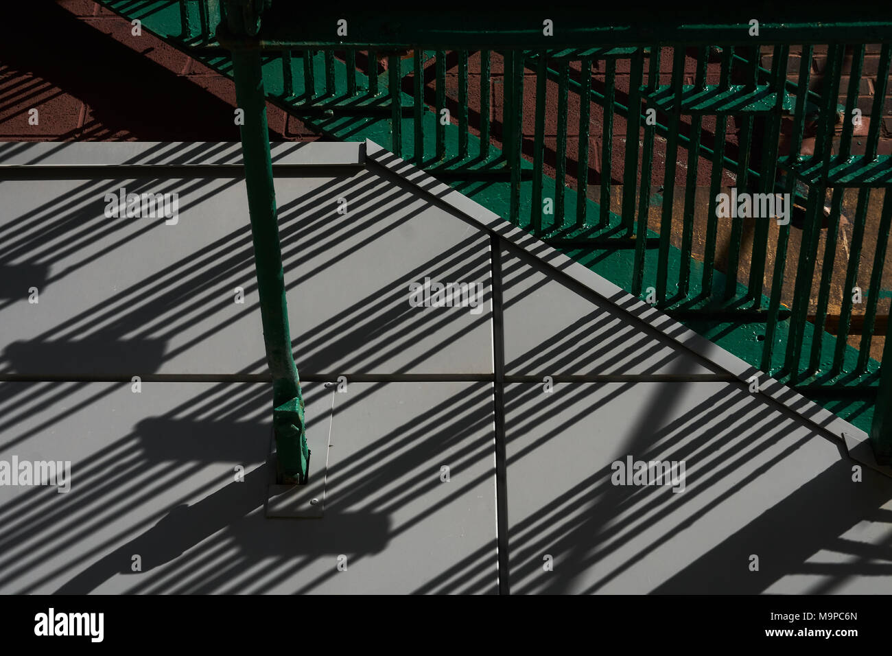 Cast diagonal line shadow patterns from a iron railing onto a sidewalk Stock Photo