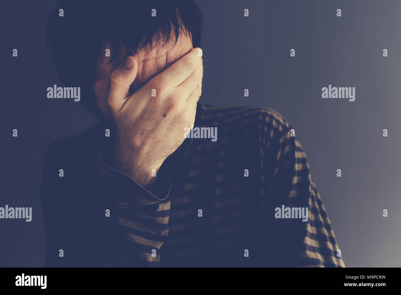Man crying alone, low key portrait with selective focus Stock Photo