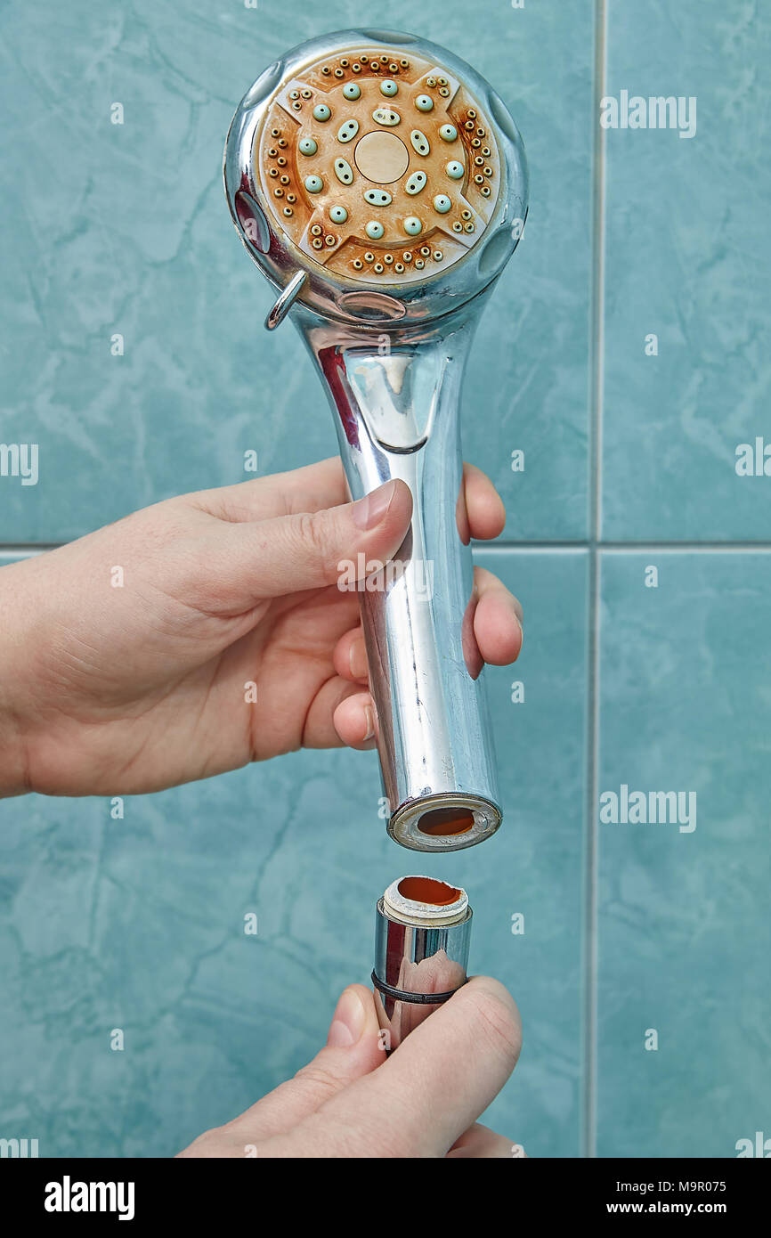 Woman is holding a broken shower head in her hands, which is detached