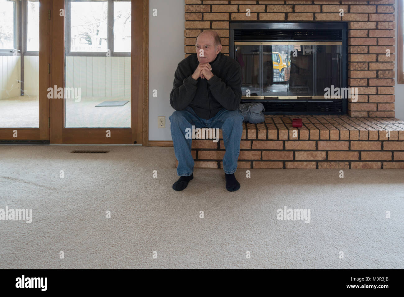 80 year old adult Caucasian man with dementia, showing sadness, observes his empty house while waiting for moving van. Wichita, Kansas, USA. Stock Photo