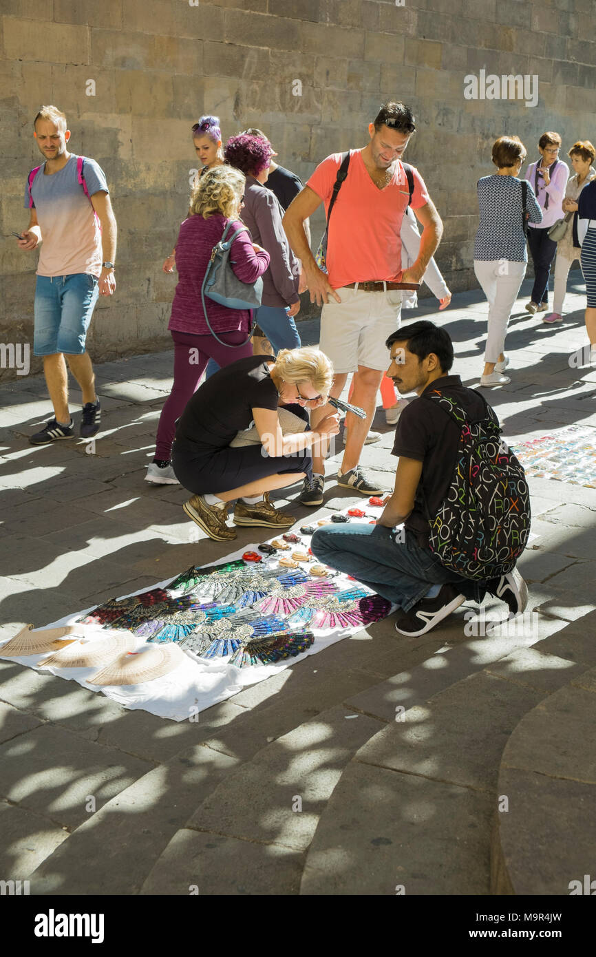 Passers-by stop to look at souvenirs sold by a street vendor in the Barri Gotic district of Barcelona Stock Photo