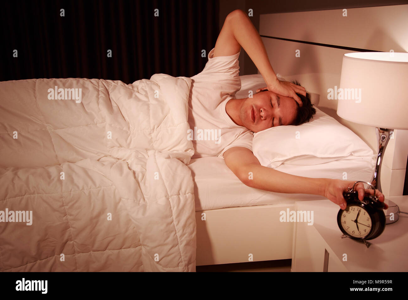 unhappy man being awakened by an alarm clock in his bedroom in the morning Stock Photo