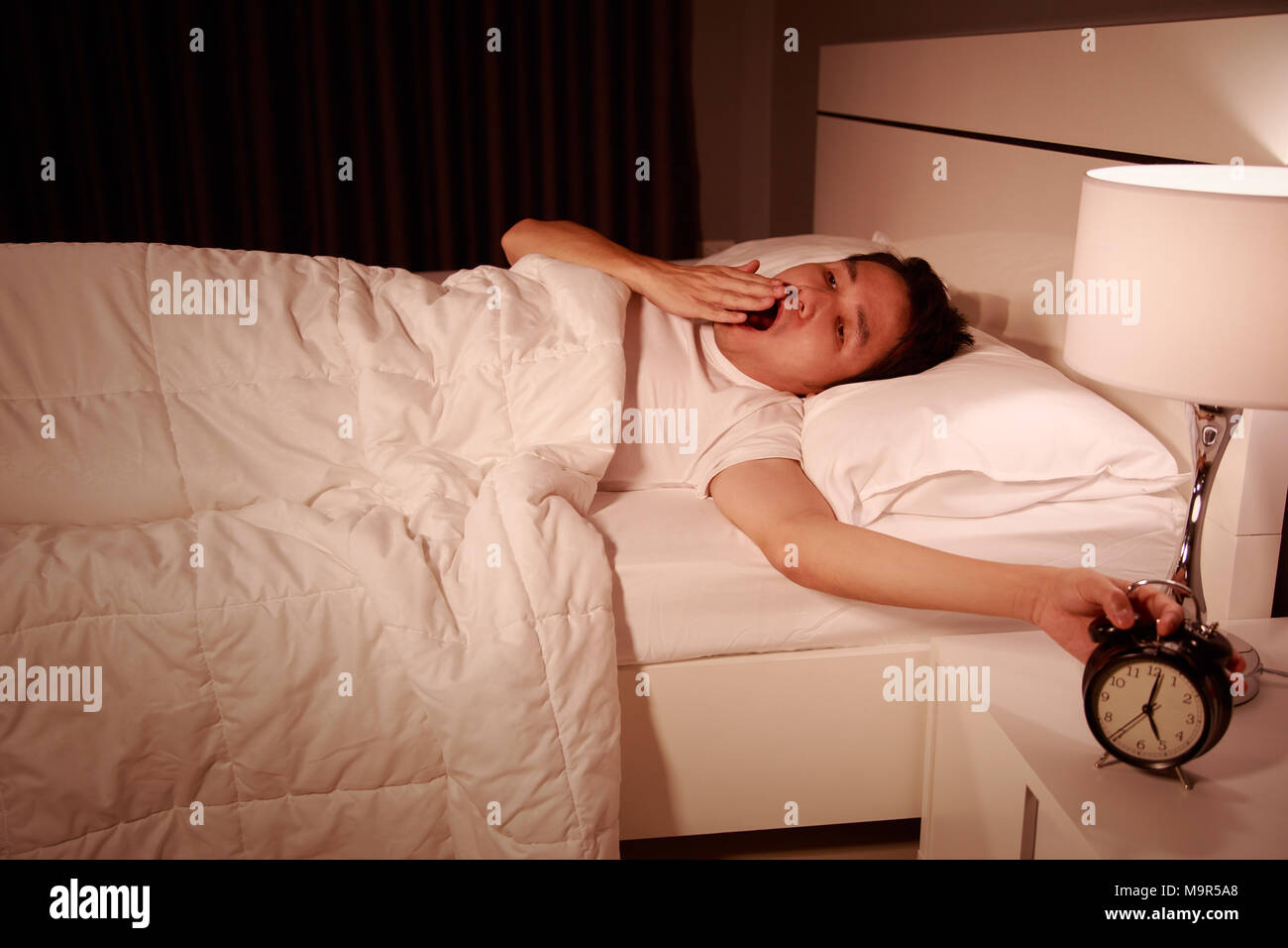 yawning man being awakened by an alarm clock in his bedroom in the morning Stock Photo