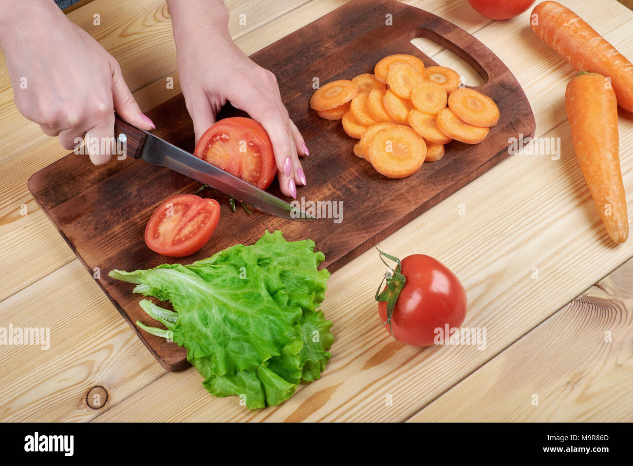 close up of female hand cutting tomato on cutting board at home, cooking, food and home concept Stock Photo