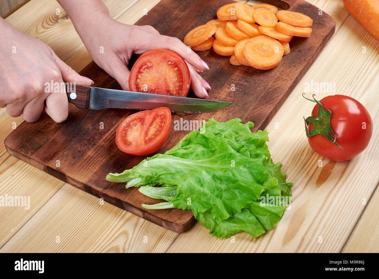 close up of female hand cutting tomato on cutting board at home, cooking, food and home concept Stock Photo