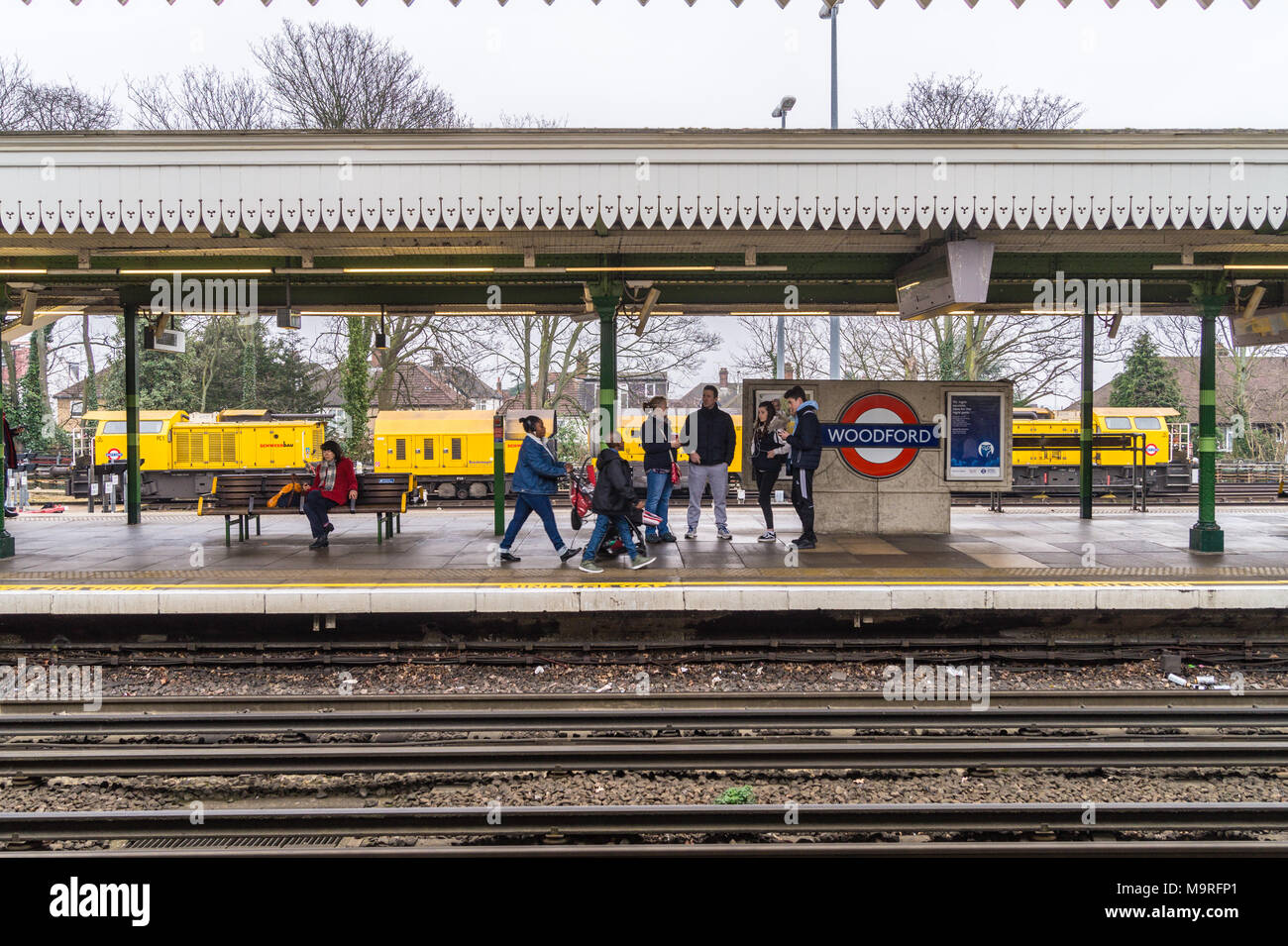 Passengers on the platform in front of a Schweerbau rail milling train parked in a siding at Woodford Underground station, Essex, England Stock Photo