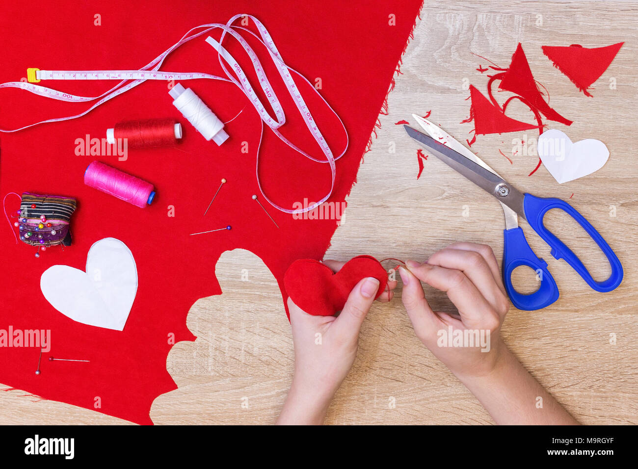 top view of hands sewing heart pattern cut from red fabric. sewing