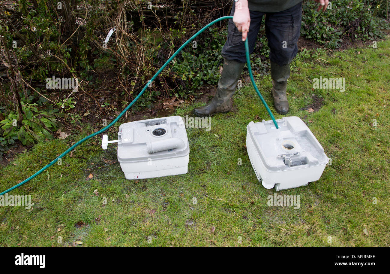 Woman using garden hose water pipe to wash clean camping toilet