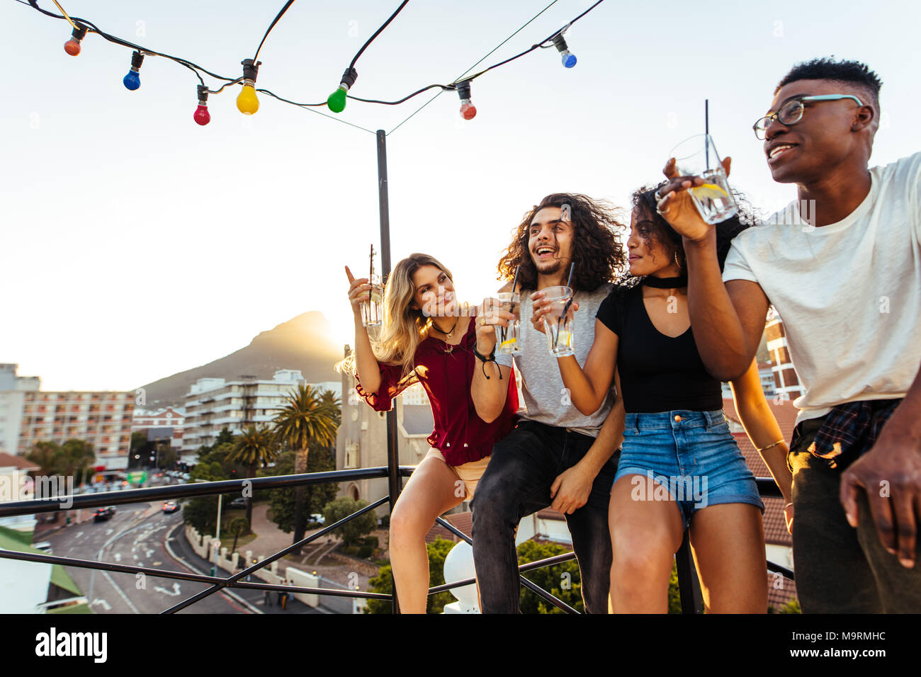 Multi-ethnic men and woman enjoying and drinking during rooftop party. Group of young friends having fun at terrace party. Stock Photo