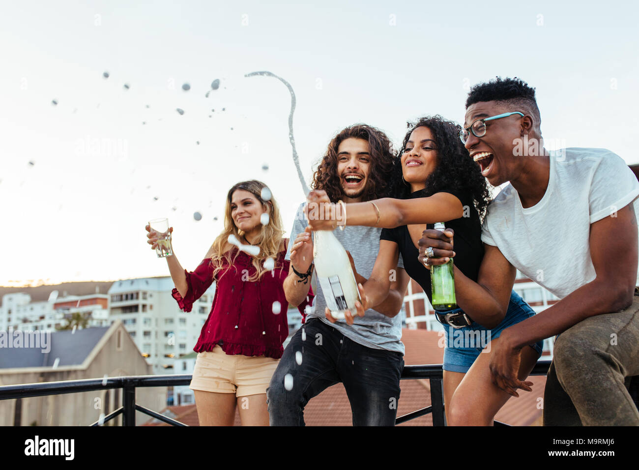 Friends opening a bottle of champagne on rooftop. Young people having champagne at terrace party. Stock Photo