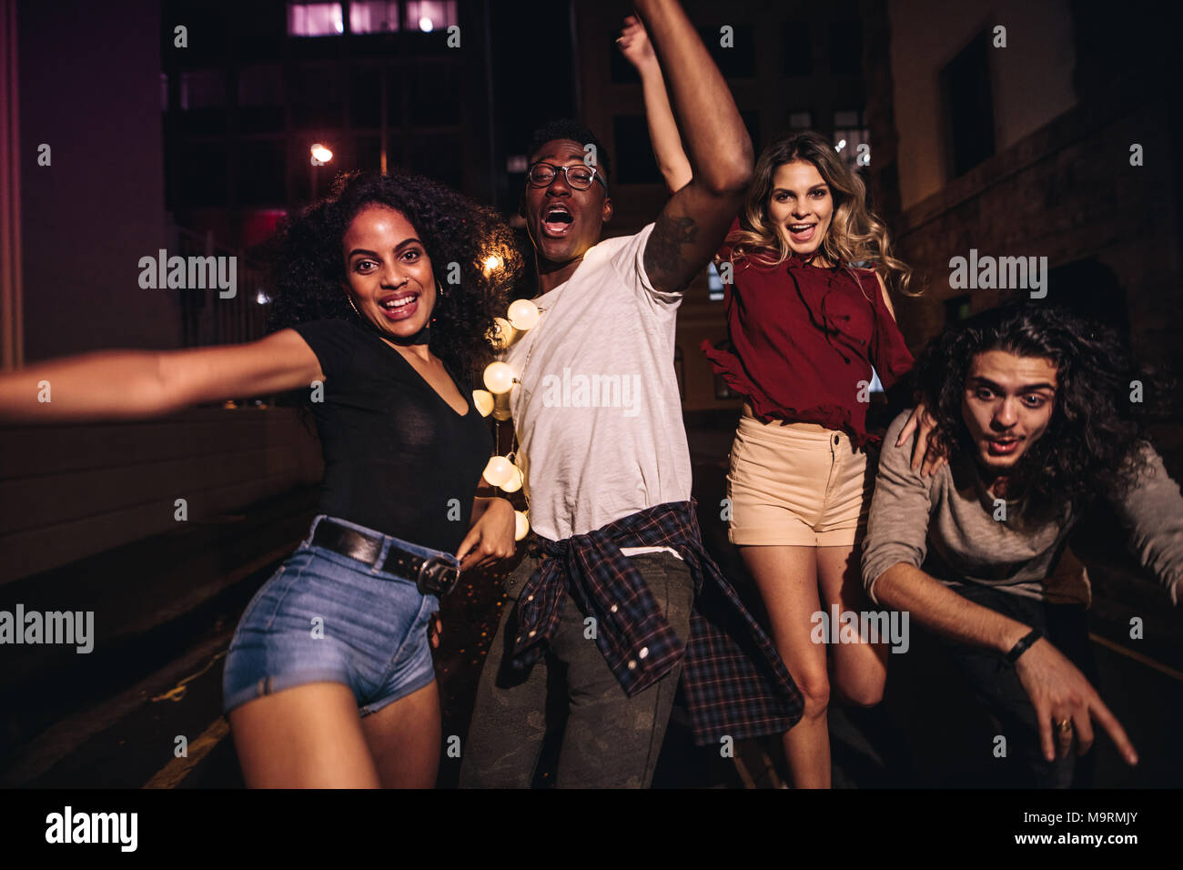 Group of multiracial friends enjoying outdoor party in the city street at night. Men and woman having fun on the street. Stock Photo