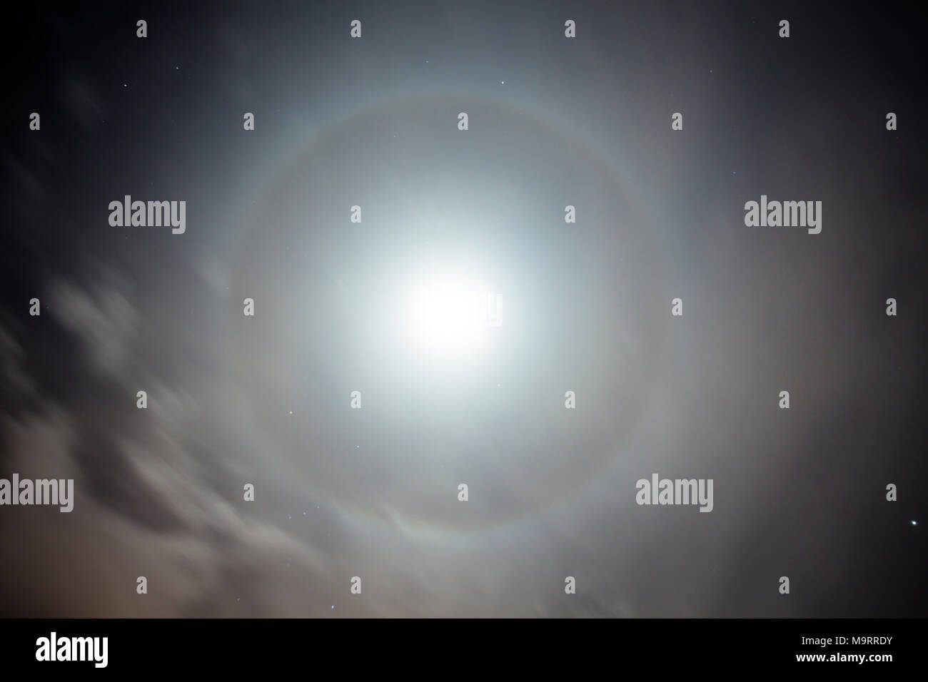 A 22° halo around the moon at night. Stock Photo