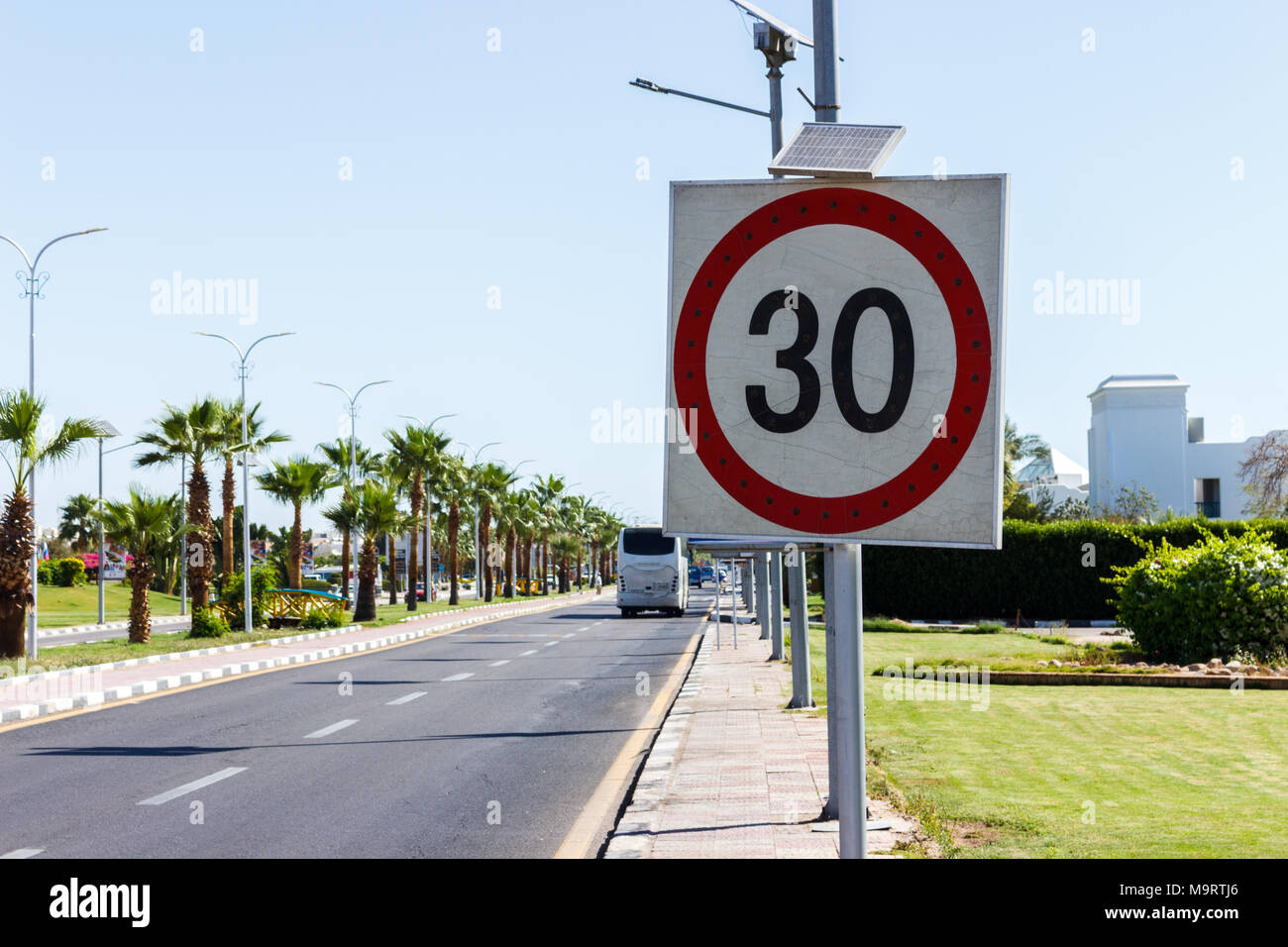 Speed limit sign with solar panel in the road with palm tree on a summer day. The speed limit is 30 km/h on a gravel road. Stock Photo