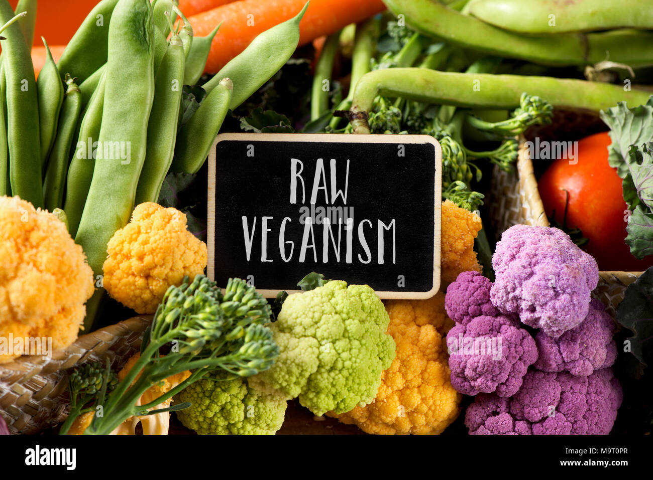 a signboard with the text raw veganism placed on a pile of some different raw vegetables, such as cauliflower of different colors, broccolini, fava be Stock Photo