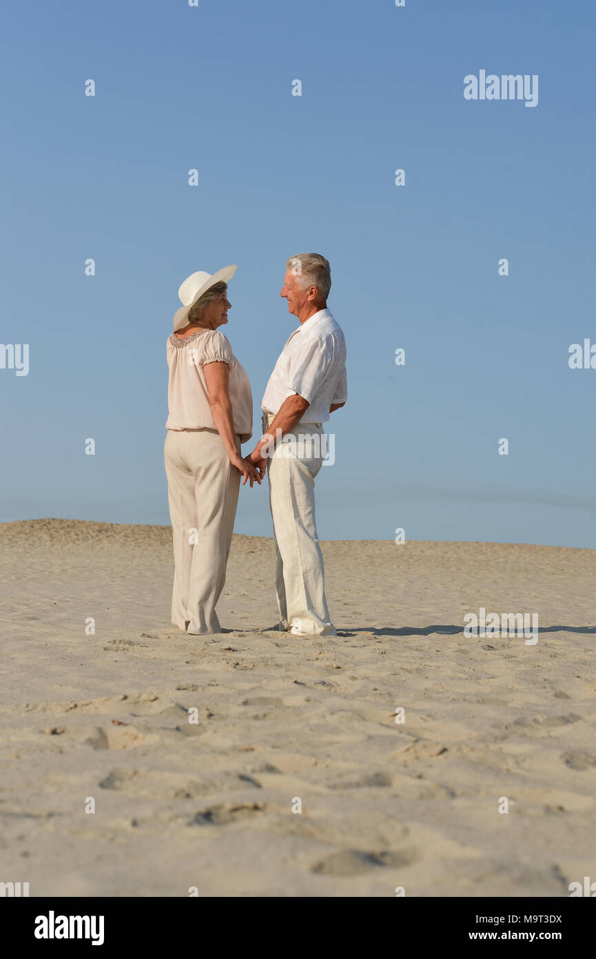 elderly couple in love walking barefoot in the sand Stock Photo