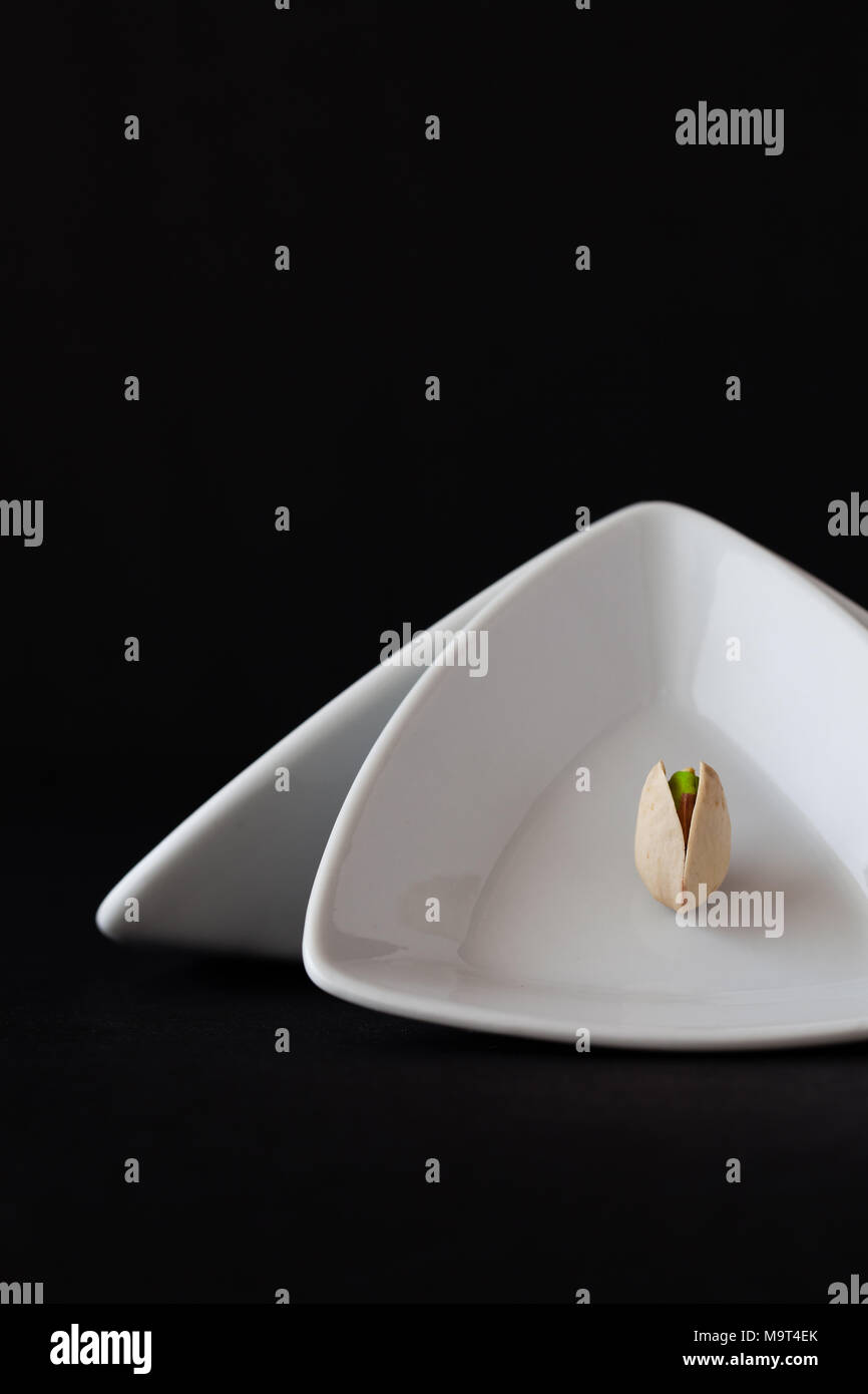 White triangular ceramic bowls with pistachio nut on the black background. Dark Food Photography