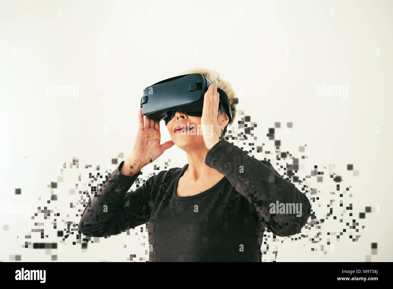 An elderly woman in virtual reality glasses is scattered by pixels. Conceptual photography with
