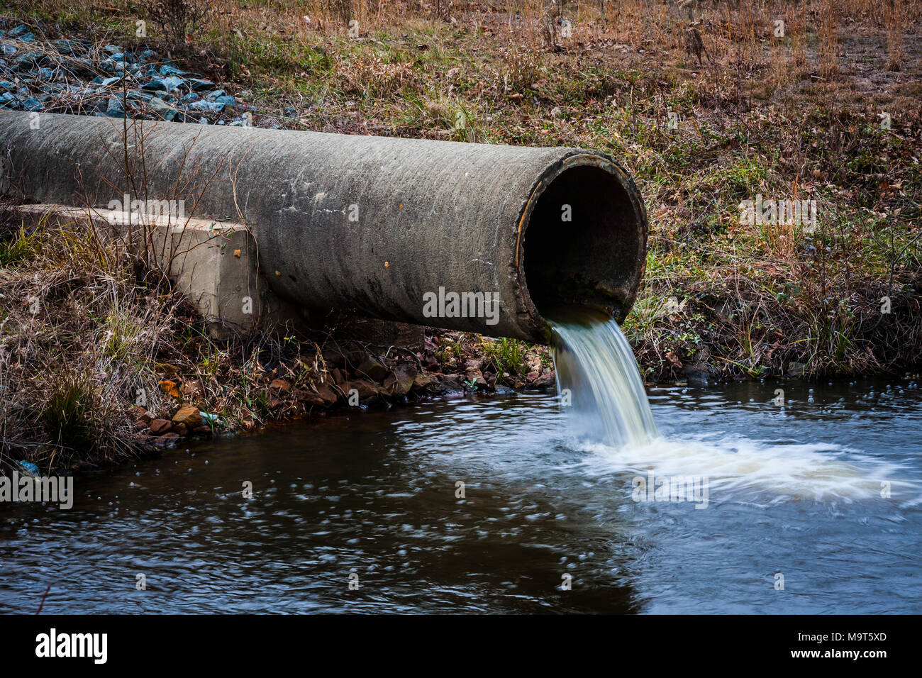 A pipe coming out of a hillside dumping liquid into a larger pond Stock