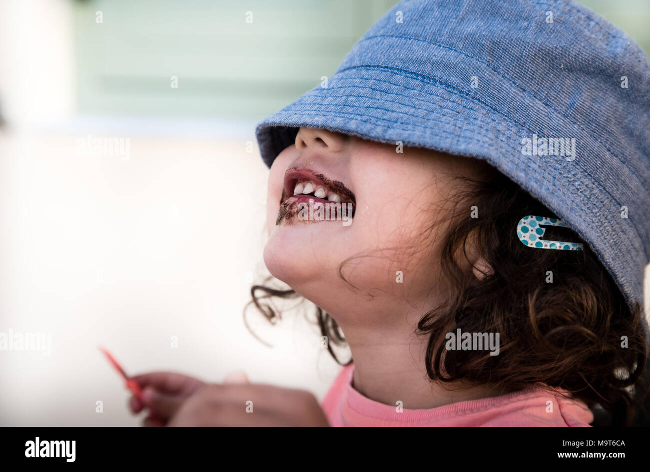 Little girl eats an ice-cream while hiding her eyes under the hat Stock Photo