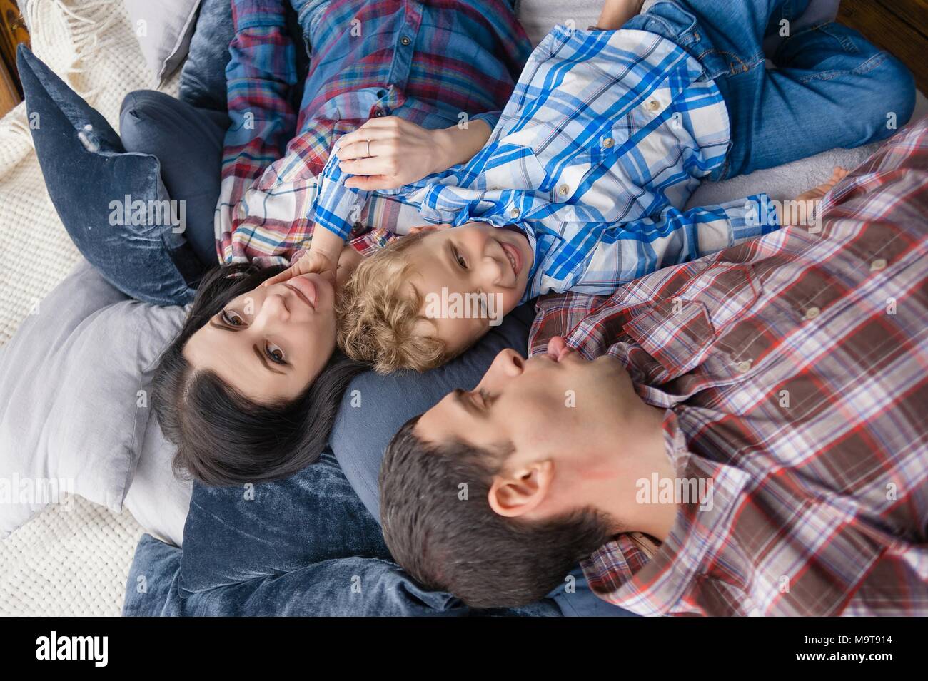 Top view of cute little boy and his beautiful young parents looking at camera and smiling while lying on the floor at home Stock Photo