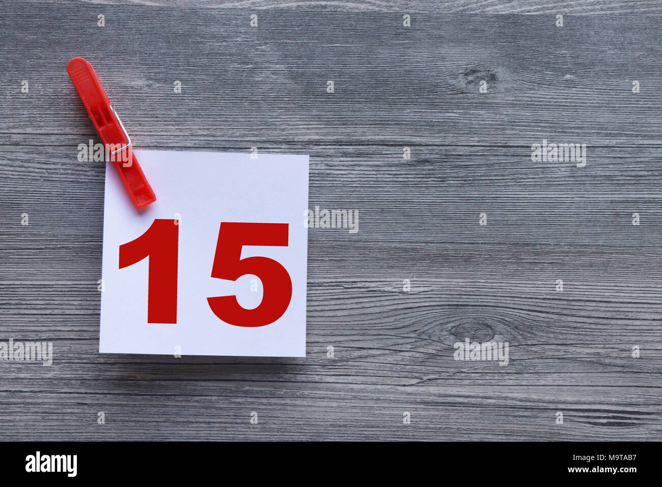 Series of red numbers on white note paper, held by red clothes peg, on grey plank background with space for copy Stock Photo