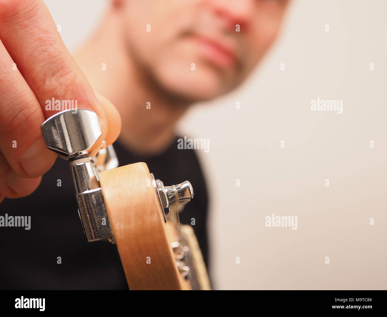 Young guitarist tuning his electric guitar in a studio, selective focus on the machine head of the guitar Stock Photo