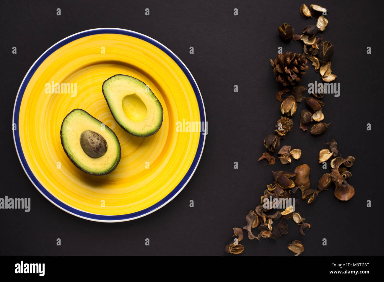 Single, sliced avocado on yellow plate. Shot top down. Member of Lauraceae family. Stock Photo
