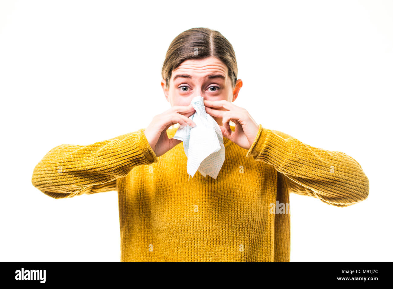 A young Caucasian woman girl wearing a yellow jumper sweater,  suffering from cold or influenza, sneezing ,  blowing her nose into a paper handkerchief, UK Stock Photo