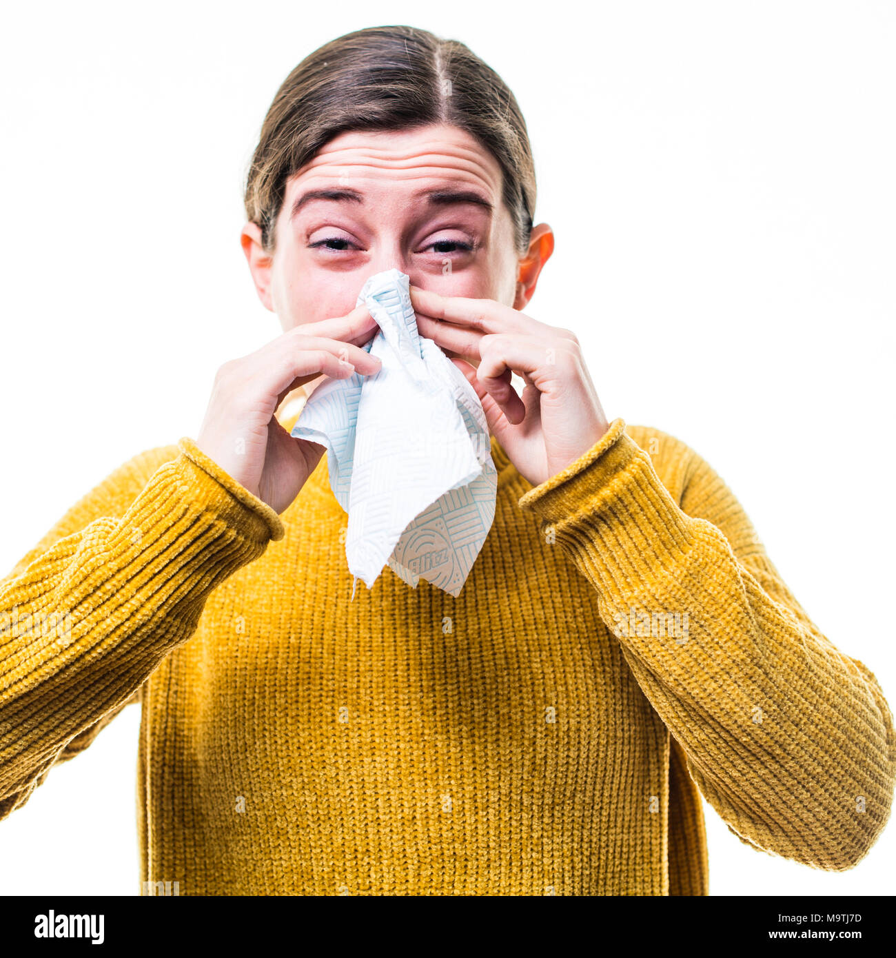 A young Caucasian woman girl wearing a yellow jumper sweater,  suffering from cold or influenza, sneezing ,  blowing her nose into a paper handkerchief, UK Stock Photo